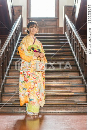 A Japanese woman in a furisode kimono stands in front of the staircase of a retro Western-style mansion (coming-of-age ceremony, coming of age, new adult). A Japanese woman in a furisode kimono stands in front of the staircase of a retro Western-style mansion (coming-of-age ceremony, coming of age, new adult). 139155985