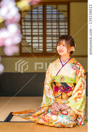 A young Japanese woman in a furisode kimono sits on the tatami mat in a Japanese-style room (coming-of-age ceremony, 20th birthday celebration). A young Japanese woman in a furisode kimono sits on the tatami mat in a Japanese-style room (coming-of-age ceremony, 20th birthday celebration). 139156015