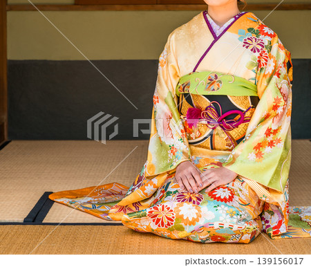A young Japanese woman in a furisode kimono sits on the tatami mat in a Japanese-style room (coming-of-age ceremony, 20th birthday celebration). A young Japanese woman in a furisode kimono sits on the tatami mat in a Japanese-style room (coming-of-age ceremony, 20th birthday celebration). 139156017