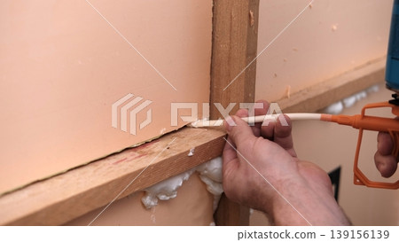 Applying thermal insulation foam with a gun. Using polyurethane foam along wall joints. Expanding the material. Sealing joints and soundproofing walls. Interior renovation. Close-up. Copy space. Applying thermal insulation foam with a gun. Using polyurethane foam along wall joints. Expanding the material. Sealing joints and soundproofing walls. Interior renovation. Close-up. Copy space. 139156139