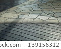 The scene of sunlight and shadows falling on the wooden deck and the stone pavement. 139156312