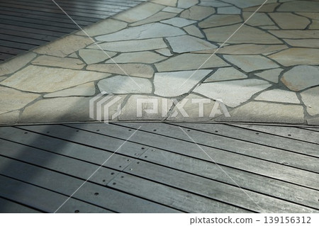 The scene of sunlight and shadows falling on the wooden deck and the stone pavement. 139156312