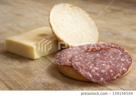 Sliced salami on sesame bun with swiss cheese block on wood Sliced salami on sesame bun with swiss cheese block on wood 139156584