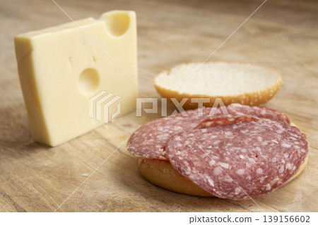 Sliced salami on sesame bun with swiss cheese block on wood Sliced salami on sesame bun with swiss cheese block on wood 139156602