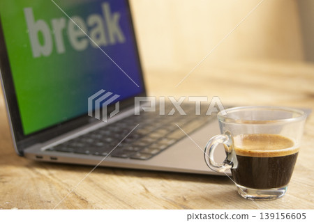 Espresso coffee cup on wooden desk next to laptop with break on screen 139156605