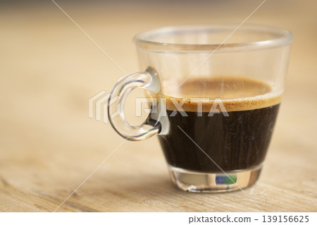 Close up of glass espresso cup with golden crema on wooden table Close up of glass espresso cup with golden crema on wooden table 139156625