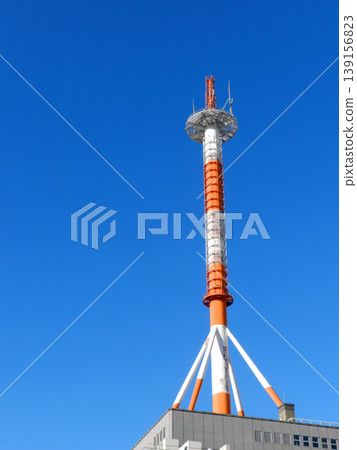 A red and white painted steel tower on a building rooftop against a blue sky. A red and white painted steel tower on a building rooftop against a blue sky. 139156823