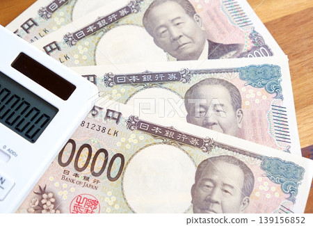 A 10,000 yen bill and a calculator - A 10,000 yen bill and a calculator placed on a table. A 10,000 yen bill and a calculator - A 10,000 yen bill and a calculator placed on a table. 139156852