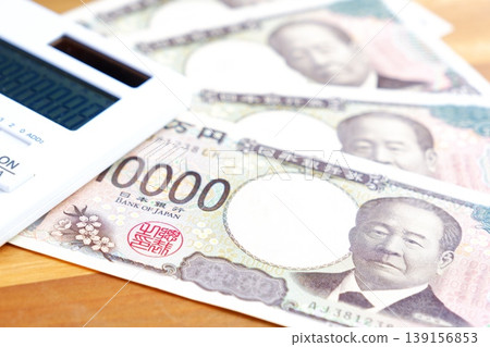 A 10,000 yen bill and a calculator - A 10,000 yen bill and a calculator placed on a table. A 10,000 yen bill and a calculator - A 10,000 yen bill and a calculator placed on a table. 139156853