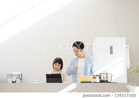 A father and daughter cooking together while looking at a tablet. A father and daughter cooking together while looking at a tablet. 139157108