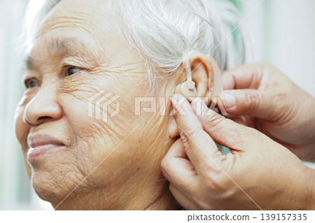 Doctor install hearing aid on senior patient ear to reduce hearing loss problem. Doctor install hearing aid on senior patient ear to reduce hearing loss problem. 139157335