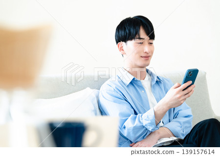 A man who uses a smartphone in the living room A man who uses a smartphone in the living room 139157614