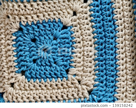 Close-up of colorful handmade granny square crochet pattern in blue and beige yarn. 139158242