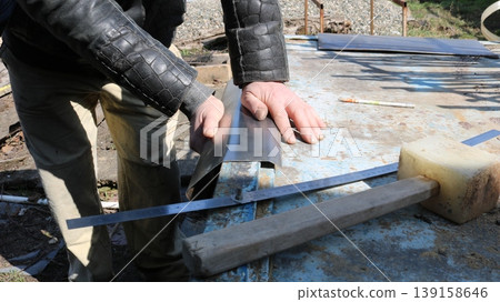 Strong male hands bend small sheets of metal on an outdoor workbench, with tools nearby, manual metalworking in a workshop, bending a piece of metal along the edge of a tabletop Strong male hands bend small sheets of metal on an outdoor workbench, with tools nearby, manual metalworking in a workshop, bending a piece of metal along the edge of a tabletop 139158646