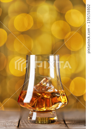 Whiskey glass with ice on wooden table and golden bokeh lights in the background Whiskey glass with ice on wooden table and golden bokeh lights in the background 139158802