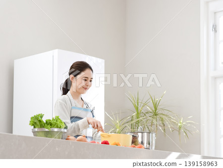A woman in an apron cooking in the kitchen A woman in an apron cooking in the kitchen 139158963