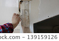 A spatula in the hand of a person repairing a wall under the ceiling above a doorway in a room near a rounded corner, patching a hole or gap when installing a room divider. 139159126