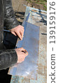 Marking out and measuring the required dimensions on a small sheet of metal lying on a work surface in an outdoor craft workshop, using a pencil and ruler in the hands of a craftsman marking out 139159176