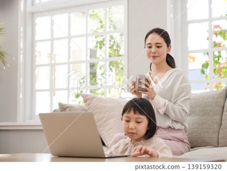A child using a laptop in the living room, with their mother watching over them. A child using a laptop in the living room, with their mother watching over them. 139159320