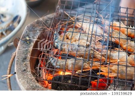 Close up of fresh river prawns grilling on charcoal stove with glowing embers and smoke Thai street food style rich flavor seafood cooking and outdoor dining atmosphere 139159629