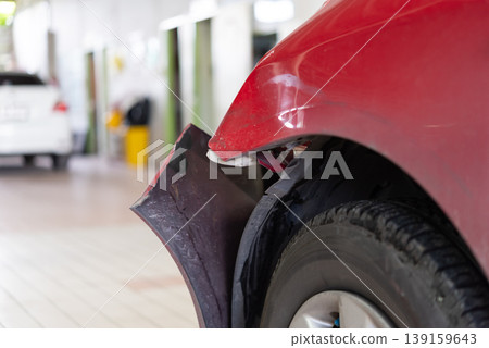 Close up of red car with damaged fender and bumper showing impact dent repair need in garage environment vehicle body damage and insurance concept Close up of red car with damaged fender and bumper showing impact dent repair need in garage environment vehicle body damage and insurance concept 139159643