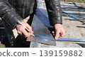 Marking a small sheet of iron on an outdoor workbench using a metallic ruler and a pencil, taking measurements of a part on a plane, and planning a metal object 139159882
