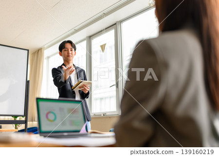 A male instructor explains while pointing to a whiteboard in an office. A male instructor explains while pointing to a whiteboard in an office. 139160219