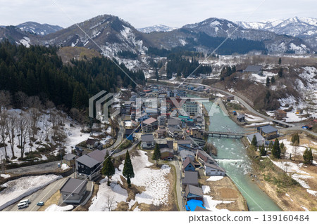 An aerial photograph taken in April of the hot spring town of Hijiori Onsen in Yamagata Prefecture, surrounded by snow-capped mountains. 139160484
