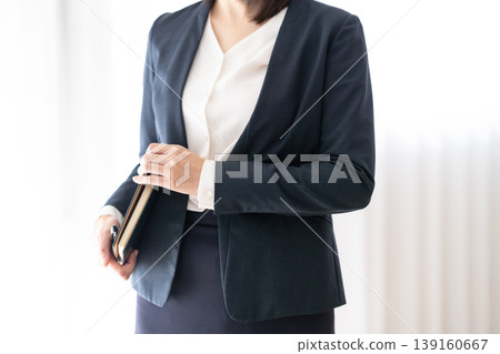 A businesswoman in a navy jacket holding a notebook and pen. A businesswoman in a navy jacket holding a notebook and pen. 139160667