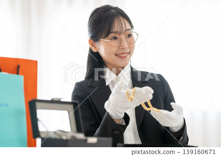 A female staff member at a specialty buying store carefully appraises precious metals. A female staff member at a specialty buying store carefully appraises precious metals. 139160671