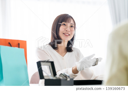 A female appraiser at a buyback shop explains things to customers with a smile. A female appraiser at a buyback shop explains things to customers with a smile. 139160673