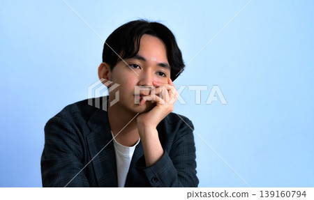 A man with a blue background and a thoughtful expression. 139160794