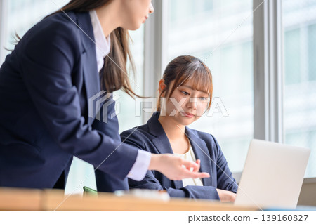 Businesswomen talking while looking at their laptops Businesswomen talking while looking at their laptops 139160827