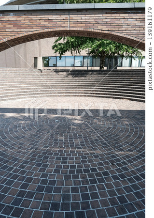 A modern architectural landscape featuring a square with a circular brick pattern and a staircase. A modern architectural landscape featuring a square with a circular brick pattern and a staircase. 139161179