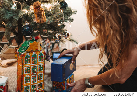 Woman placing a Christmas gift under a decorated tree at home. Cozy festive moment with wrapped presents, warm lights and holiday decor. Christmas morning, family celebration and seasonal lifestyle. Woman placing a Christmas gift under a decorated tree at home. Cozy festive moment with wrapped presents, warm lights and holiday decor. Christmas morning, family celebration and seasonal lifestyle. 139161497