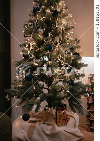 A cozy Christmas scene at home in Kyiv, Ukraine, on December 19, 2025: Presents under a decorated tree with blue ornaments and toys, symbolizing holiday joy. Vertical backdrop of cozy home decorations 139161501