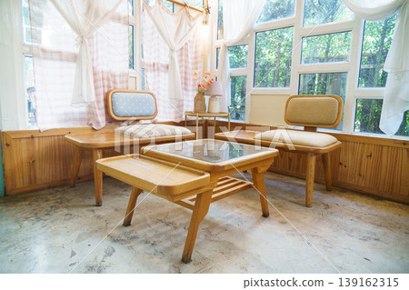 Cozy Sunlit Corner with Wooden Seating and Cushioned Chairs in Bright Room with Large Windows and Sheer Curtains 139162315