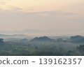 Misty mountain landscape with rolling hills and distant peaks under a soft, cloudy sky during early morning or late evening light 139162357