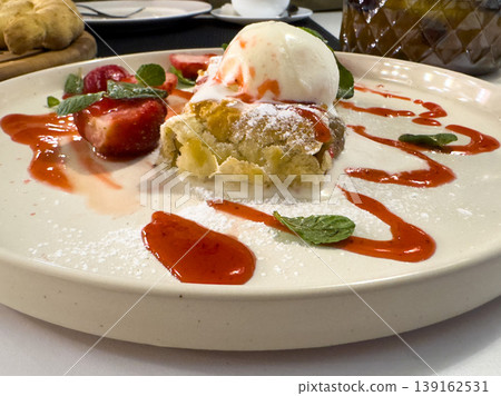 Warm apple strudel with vanilla ice cream, strawberry sauce and fresh mint, a delicious dessert Warm apple strudel with vanilla ice cream, strawberry sauce and fresh mint, a delicious dessert 139162531
