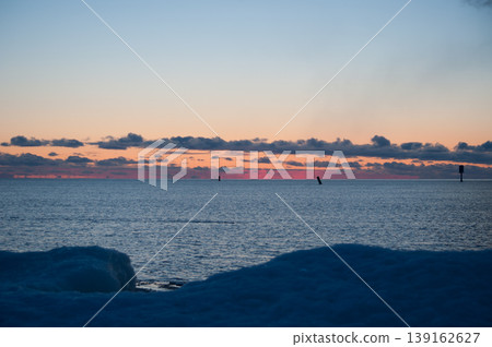 Navigational buoys in the Gulf of Bothnia near the Finnish coast with the red colors of setting sun in the horizon and packed ice in the foreground Navigational buoys in the Gulf of Bothnia near the Finnish coast with the red colors of setting sun in the horizon and packed ice in the foreground 139162627