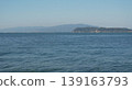 The gentle waves on the calm surface of the sea and the hazy mountains in the distance create a beautiful landscape. 139163793