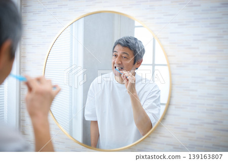 一位 60 多歲的男子一邊刷牙一邊照鏡子 139163807