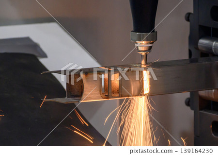 High-precision fiber laser machine engraving and cutting a square metal pipe with intense sparkling light. 139164230