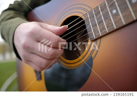 A man is playing the guitar. The guitarist gives lessons on playing a classical musical instrument. Close-up of a guy's hand fingering the strings of a guitar A man is playing the guitar. The guitarist gives lessons on playing a classical musical instrument. Close-up of a guy's hand fingering the strings of a guitar 139165191