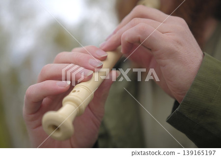 The piper plays the flute, close-up on his hands. A man holds a wooden flute in his hands. The musician is wearing a green jacket. Flute lessons. The flutist performs The piper plays the flute, close-up on his hands. A man holds a wooden flute in his hands. The musician is wearing a green jacket. Flute lessons. The flutist performs 139165197