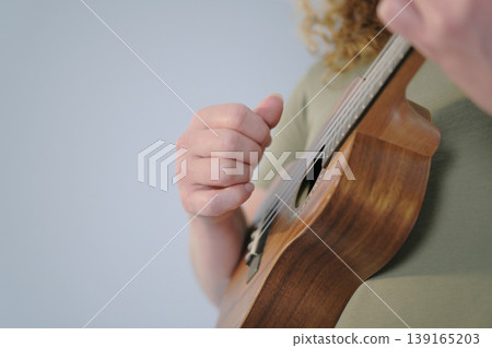 The guitarist plays the ukulele, close-up, focus on the hand. A man holds a ukulele in his hands and plays it. The concept of relaxation and enjoyment 139165203
