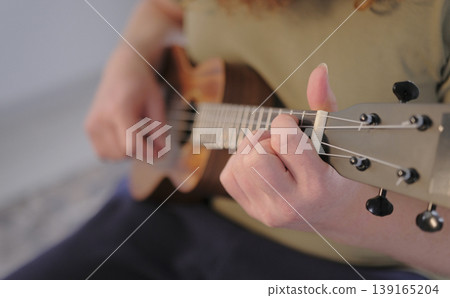 The guy plays the ukulele, close-up on his hand and strings. Ukulele lessons. A musician learns a new melody The guy plays the ukulele, close-up on his hand and strings. Ukulele lessons. A musician learns a new melody 139165204