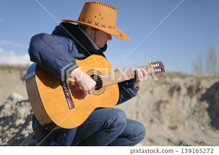 A lonely musician melancholically plays the guitar in an abandoned area on the street. A woman in a cowboy hat is learning to play the guitar. The concept of freedom and relaxation A lonely musician melancholically plays the guitar in an abandoned area on the street. A woman in a cowboy hat is learning to play the guitar. The concept of freedom and relaxation 139165272