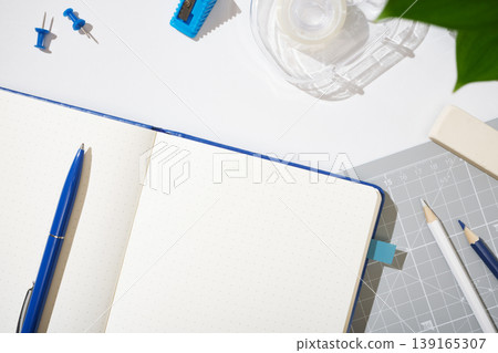 Open dotted notebook with blue pen, pencils, eraser, ruler, tape, sharpener, pins. Workspace background, copyspace. Open dotted notebook with blue pen, pencils, eraser, ruler, tape, sharpener, pins. Workspace background, copyspace. 139165307