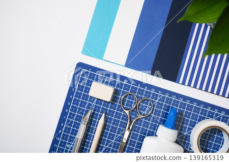 Flat lay of craft tools on a blue cutting mat. Creative workspace with scissors, hobby knife, glue, and stationery for scrapbooking, Copyspace Flat lay of craft tools on a blue cutting mat. Creative workspace with scissors, hobby knife, glue, and stationery for scrapbooking, Copyspace 139165319